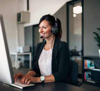 Beautiful customer representative with headset smiling during conversation with a client.